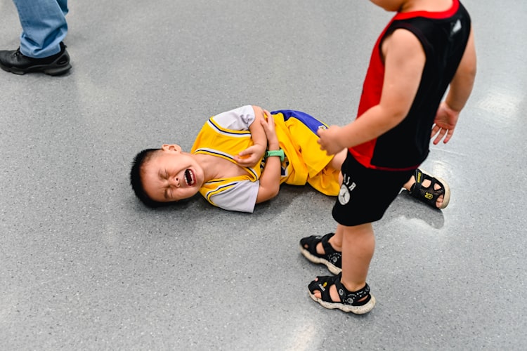 Anak berkaus basket kuning terjatuh di lantai sambil memegangi lengannya karena cedera